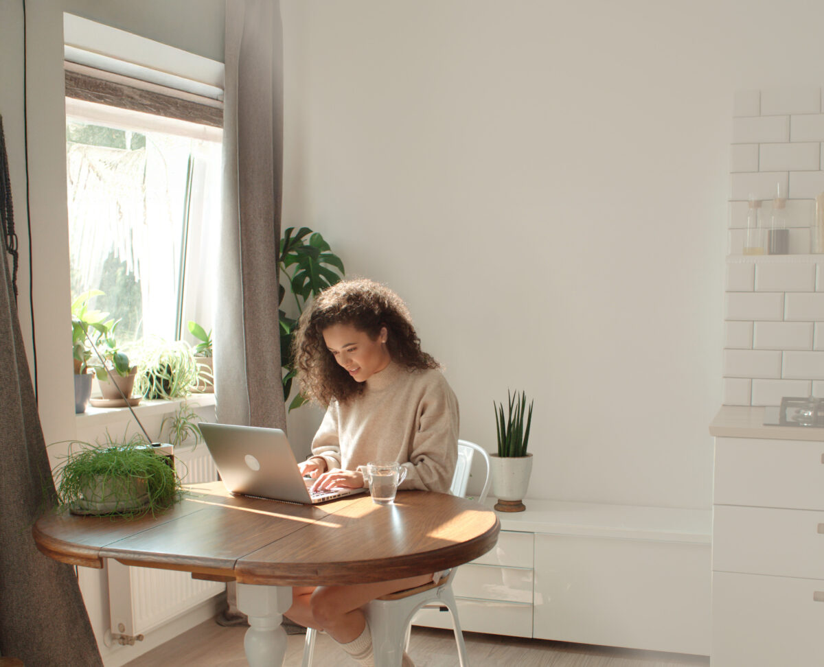Charming young woman typing on laptop computer in a kitchen.